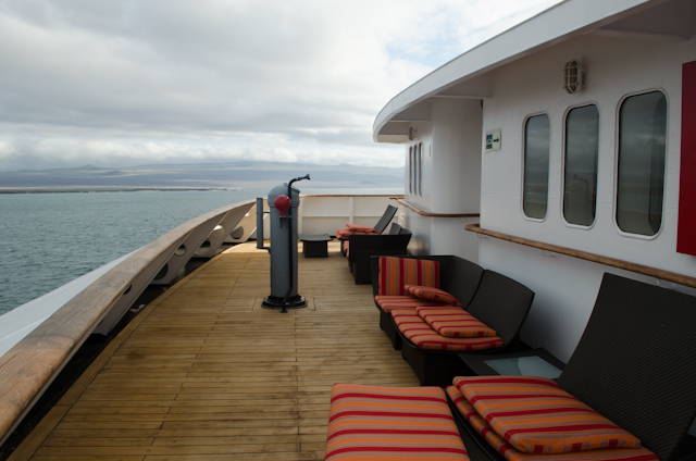 ...a forward-facing deck space on Deck 5. This is technically part of the shared balcony for Terrace Suite guests, so perhaps don't make yourself cozy in one of the loungers. At anchor, it's quite pleasant here. Underway - as seen here - the wind has a tendency to blow the cushions off the chairs. Photo © 2014 Aaron Saunders